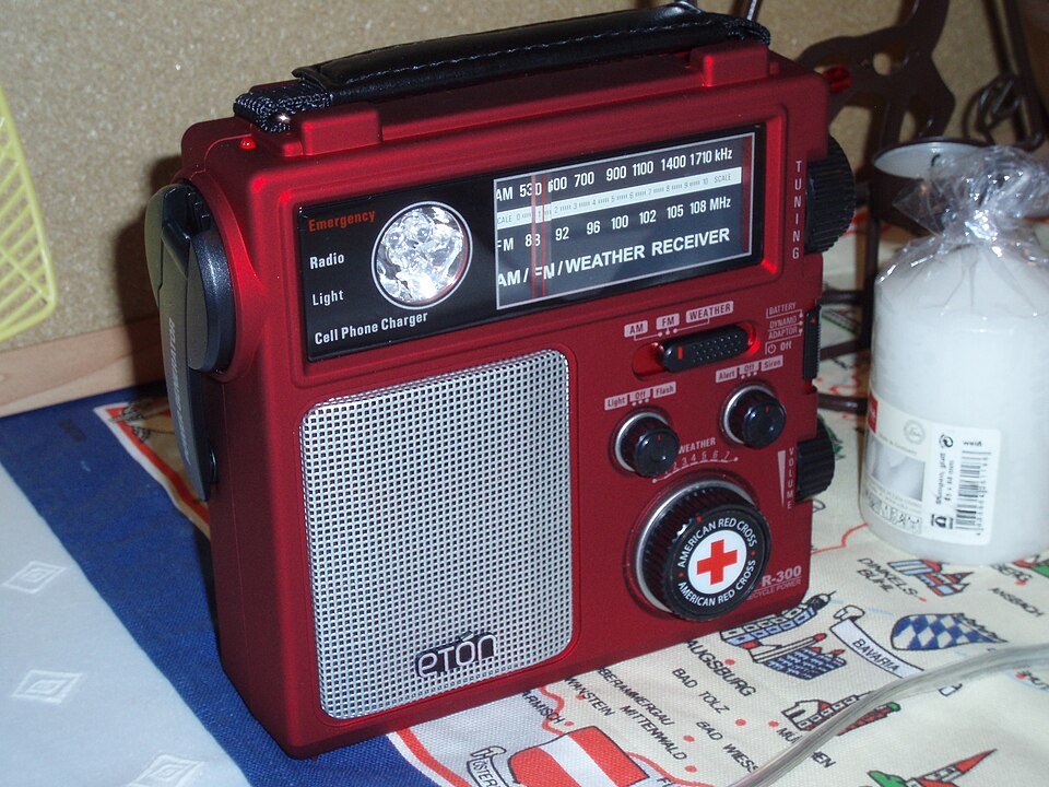 A red Eton emergency radio with a tuning dial, speaker grille and hand crank, for storm prep in Pensacola, FL